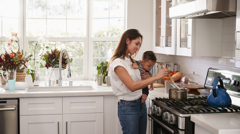 Woman holding baby while stirring pot
