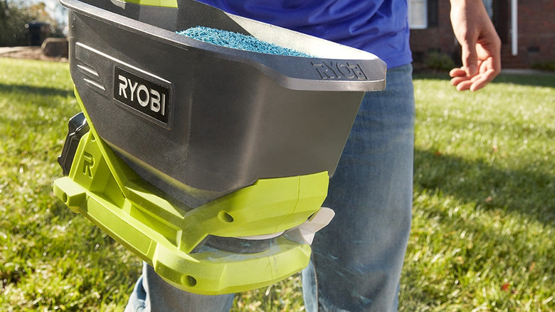 A man using a Ryobi power spreader to spread fertilizer pellets