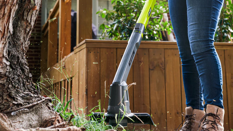 A person trimming grass near a tree with Ryobi's 18V One+ 10-inch Cordless Battery Trimmer/Edger