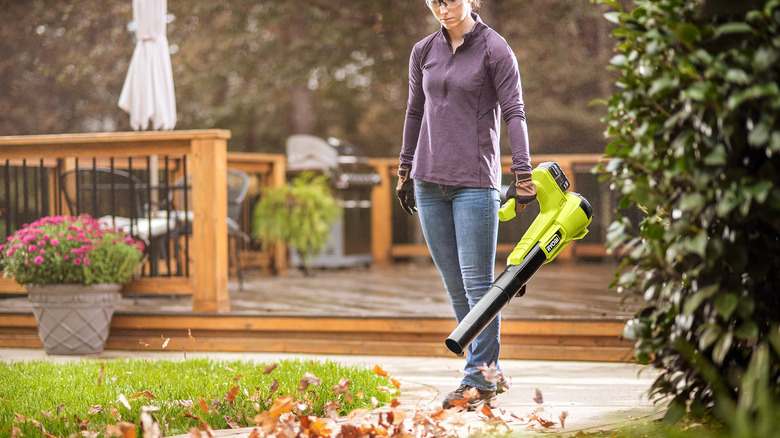 A woman cleaning her yard with Ryobi's 18V One+ Cordless Battery Leaf Blower/Sweeper