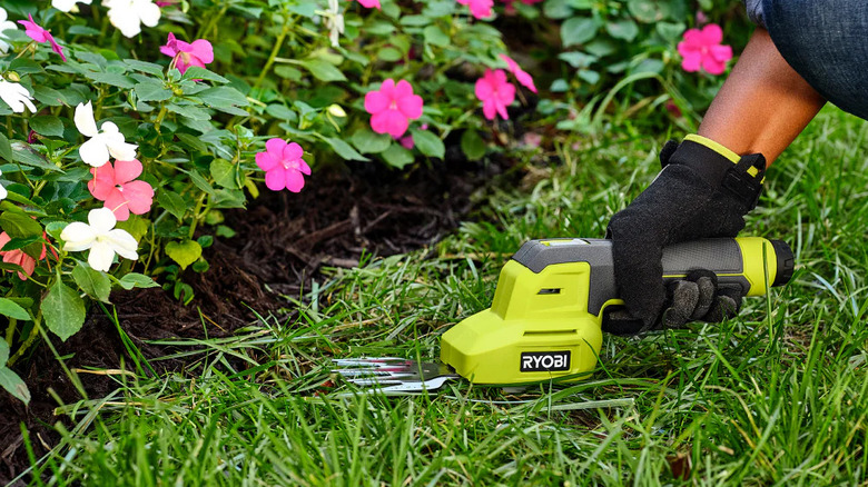A person trimming grass close to a flower bed with Ryobi's USB Lithium Shear Shrubber Kit