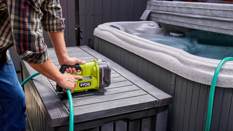 A person draining a hot tub using Ryobi's 18V One+ Cordless Transfer Pump