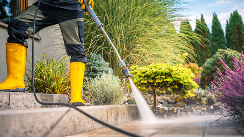 Person in boots pressure washing a garden path
