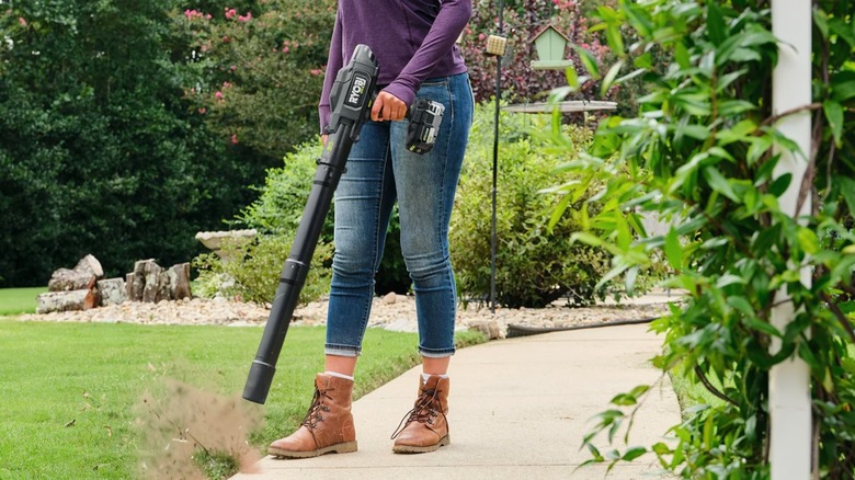a person using the RYOBI ONE+ HP Cordless Compact Leaf Blower to clean dust from the edges of a walkway