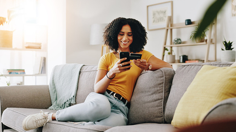 A woman on a couch holding her phone and a credit card