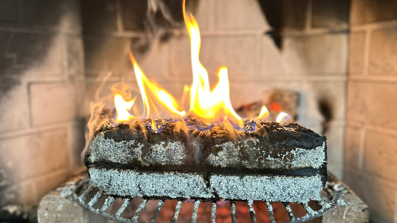 An ashy log is burning in a sooty chimney