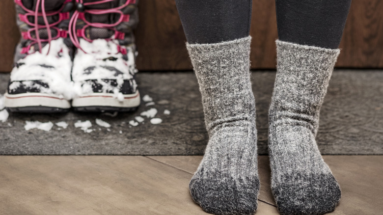 Snow covered boots are shown next to the feet of someone wearing socks