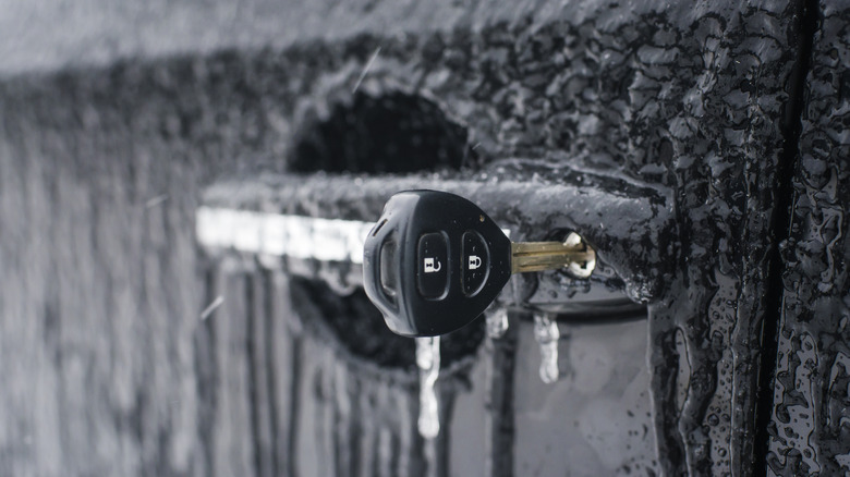 A car key is stuck in a frozen car lock, with icicles around the door handle