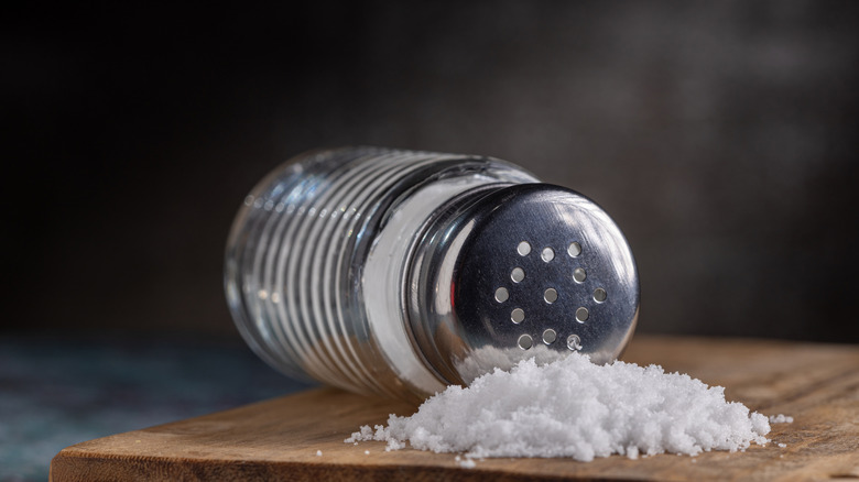 A shaker of salt is on its side, next to a large pile of spilled salt