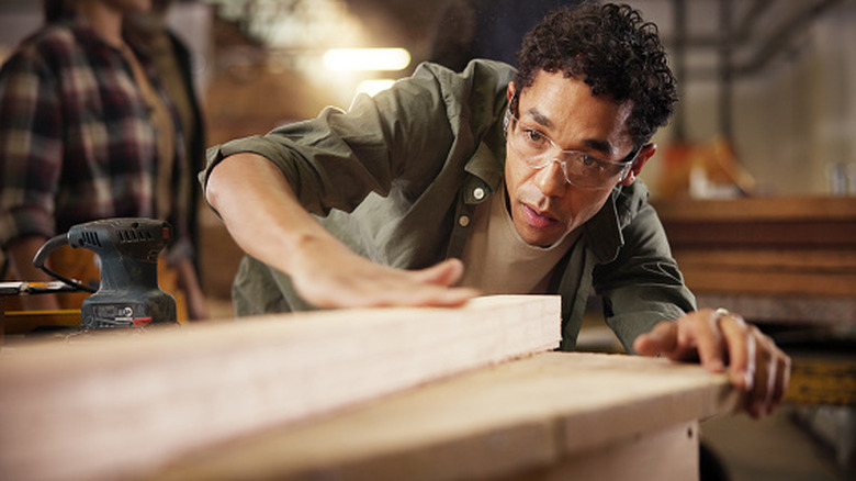 A man in workshop examining sanded piece of wood
