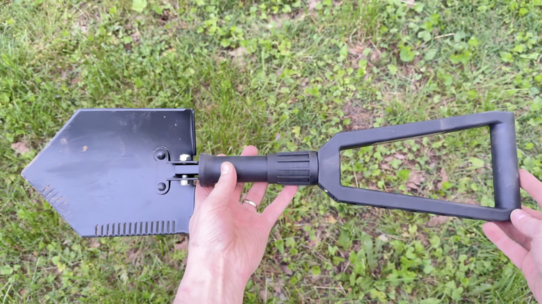 A person holding Badland's Foldable Utility Shovel in a grassy area