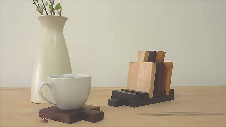 Mini wooden cutting boards displayed in a stand and under a teapcup beside a flower vase.