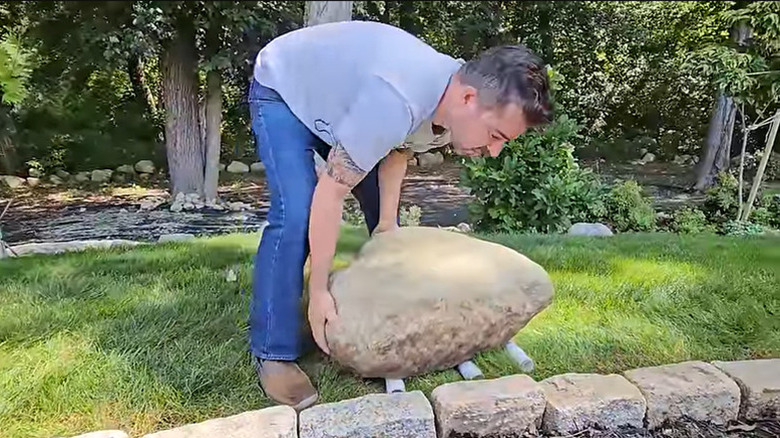 Man using PVC pipes to move large rock in yard