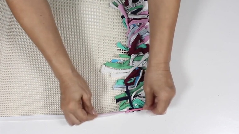 Hands tying t-shirt strips into knots in a rug pad gripper