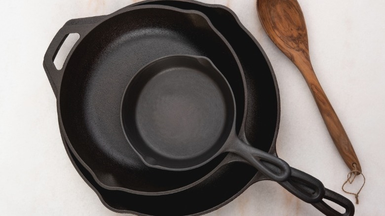 Stack of clean seasoned cast iron skillets next to a wooden spoon
