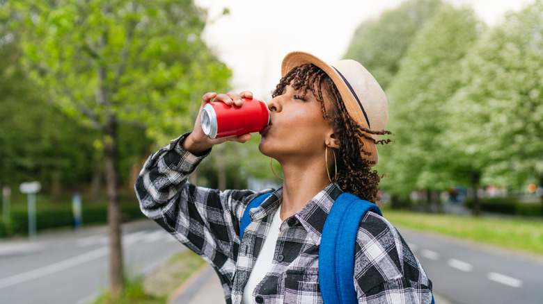 A young woman in a park drinking from a can