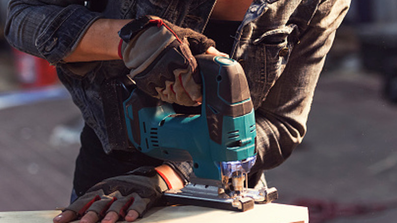 A woman cutting a curve on a piece of wood using a jigsaw
