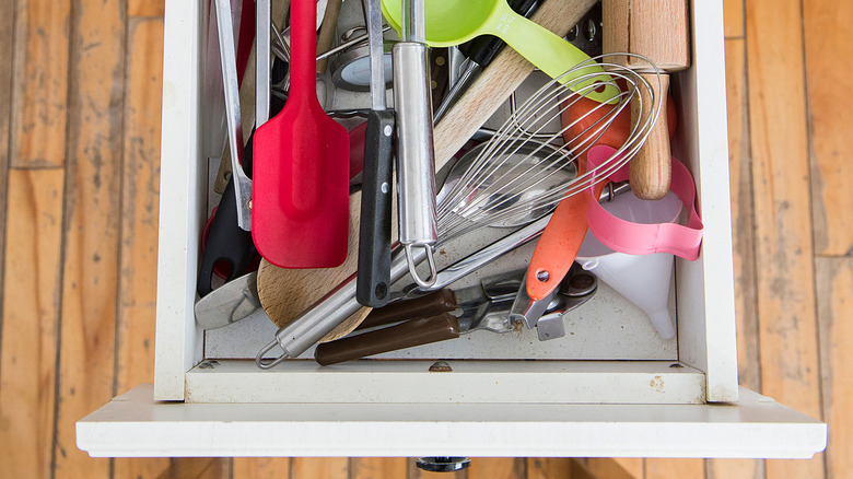 A cluttered kitchen drawer contains various utensils