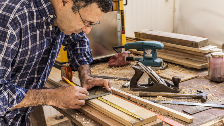 A person marks a piece of wood with a pencil in a workshop.