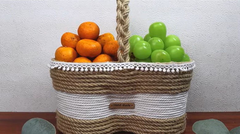 A basket made from twine and yogurt containers holds clementines and grapes.