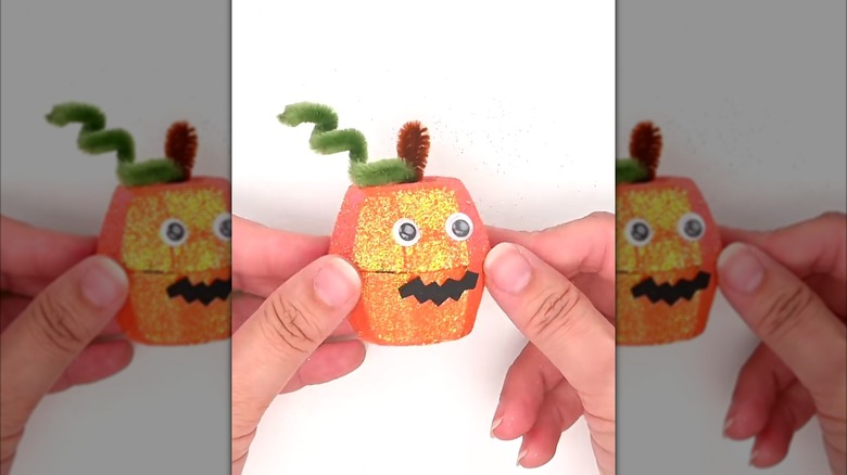 A person holding a mini orange glitter pumpkin made with two halves of egg carton cups.