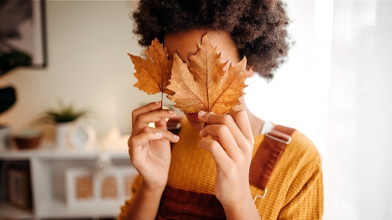 person hiding behind fall leaves