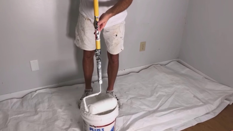person putting thinned joint compound on paint roller to skim coat wall