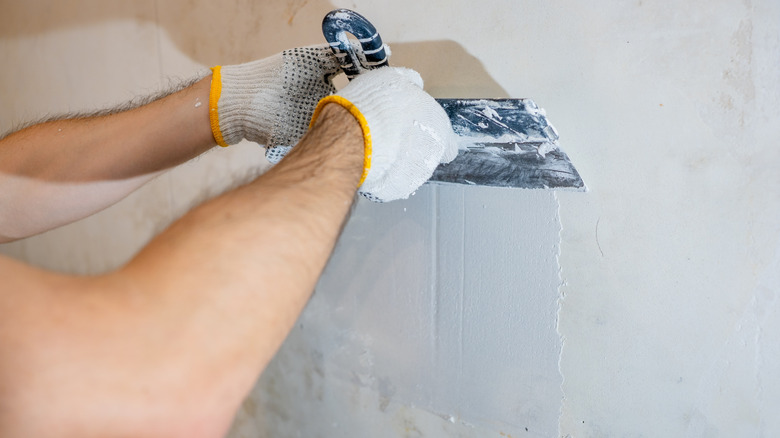 close-up of hands applying skim coat to a wall