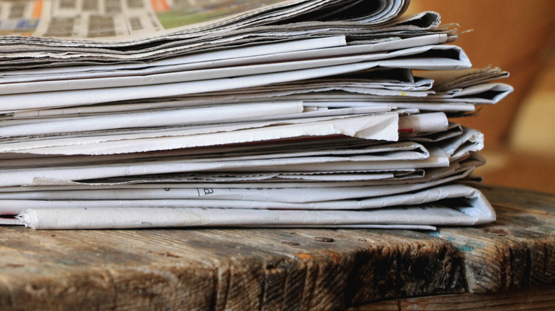 A pile of newspapers on a old wooden table.