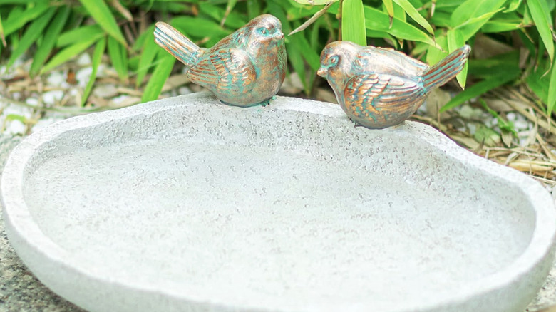 Resin bird bath with decorative birds situated on ground with water in it