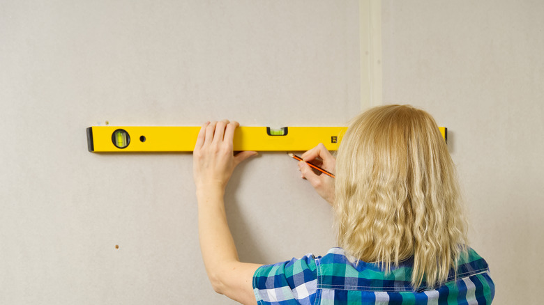woman marking drill spots on wall with level and pencil