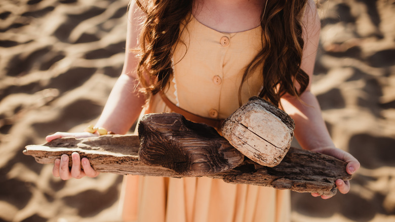 woman holding driftwood and shells on a beach