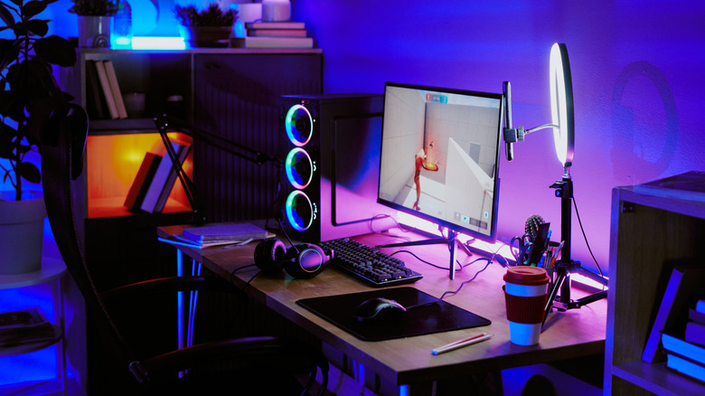 A gaming setup in the dark with lots of RGB lights around the space and the monitor and light ring on