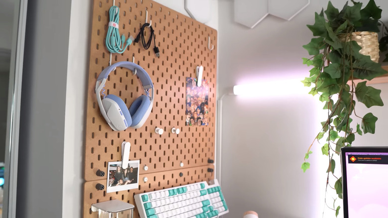 A screenshot of a video showing a pegboard next to a gaming setup with pictures, cords, and headphones onit