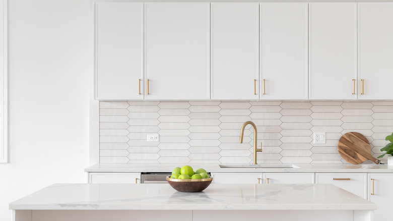 An all-white kitchen with a bowl of apples on the kitchen island