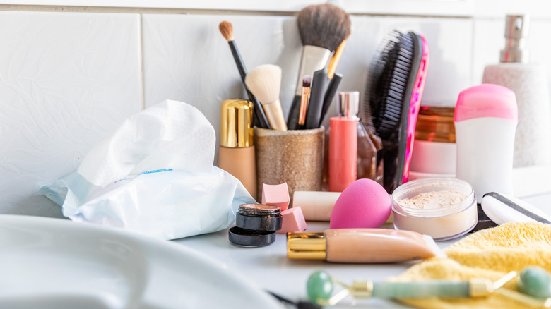 A cluttered bathroom countertop with makeup brushes and toiletries
