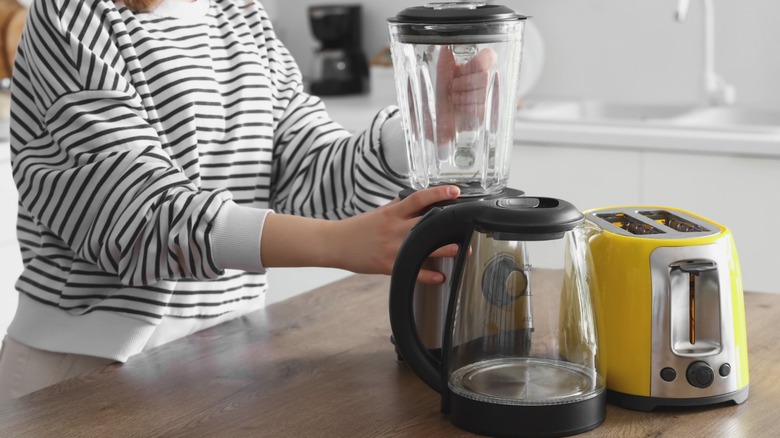 Person handling small kitchen appliances on wood counter