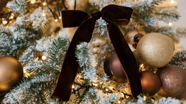 A brown velvet bow on a gold themed flocked Christmas tree