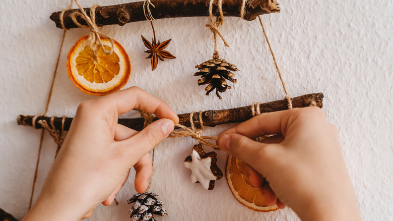 A person tying twine, dried oranges, and pine cones to sticks in the shape of a Christmas tree