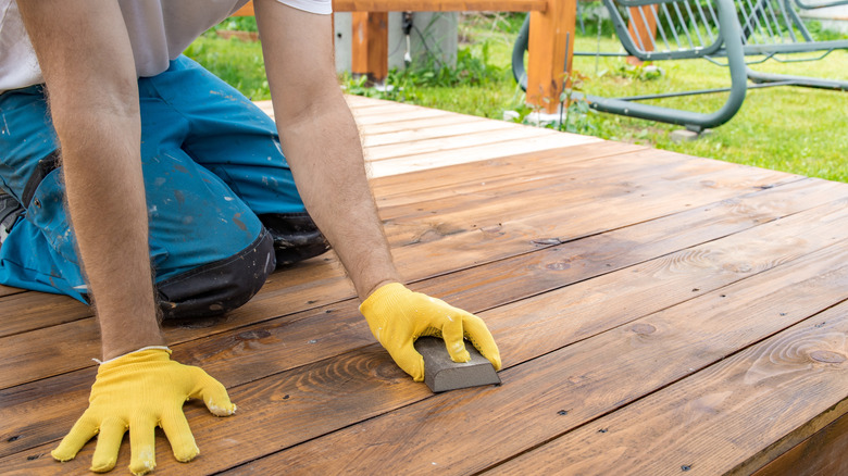 Person with gloves on staining a wooden deck
