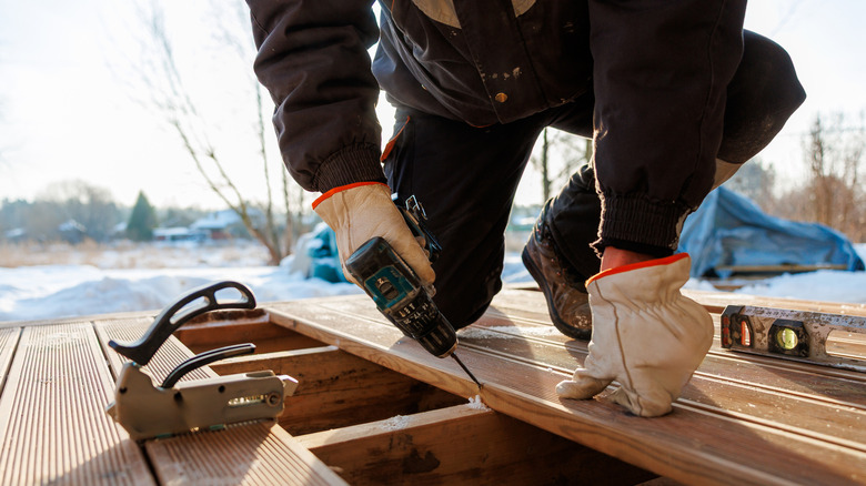 Construction worker screwing deck boards into wooden joists