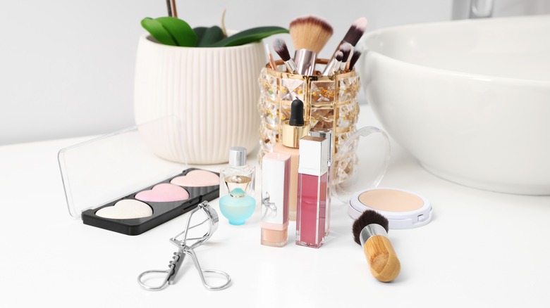 A white bathroom counter with makeup products scattered on it.