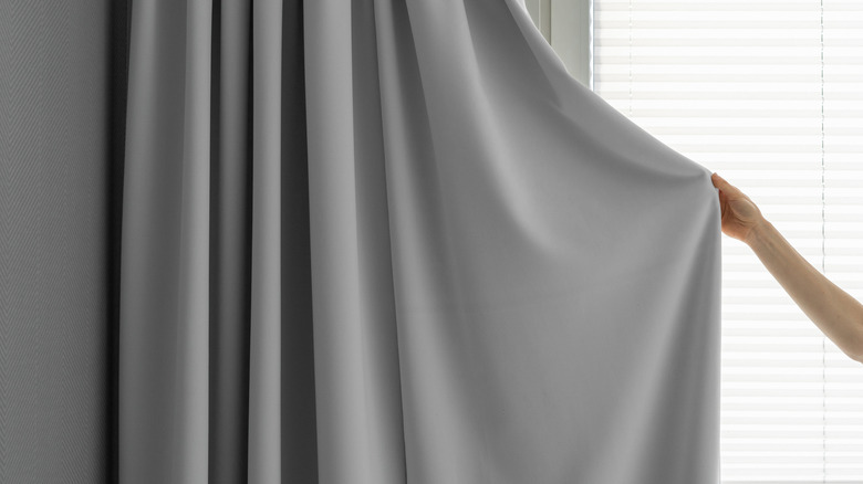 Person pulling grey curtain forward.