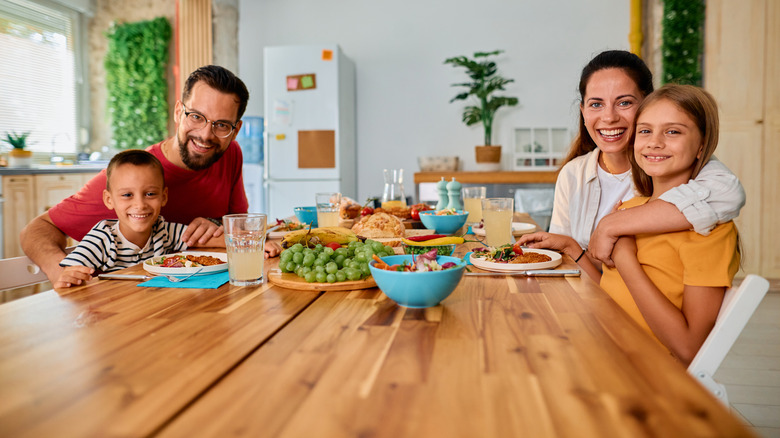 Smiling parents and their two kids sit at the dining room table before eating
