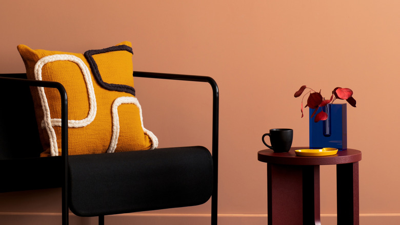 Home decor set up with warm pink walls, a black chair, yellow pillow, and dark wood side table