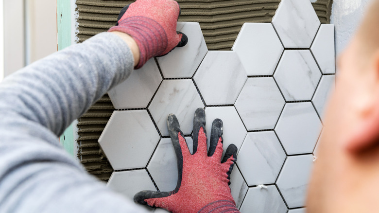 Person adding hexagon tile to a wall