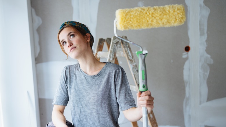 Female with paint roller contemplates unpainted room