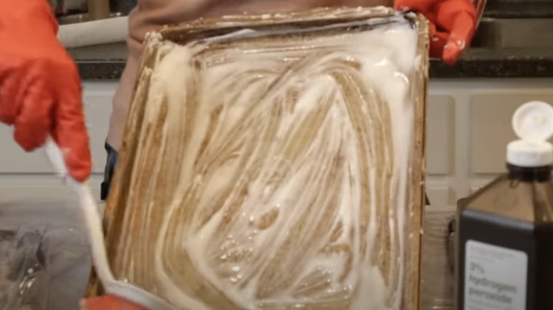 Person using a brush to scrub baking soda and hydrogen peroxide on a baking sheet