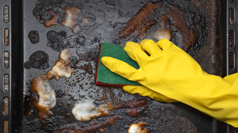 Burnt baking sheet being scrubbed by gloved hand with sponge