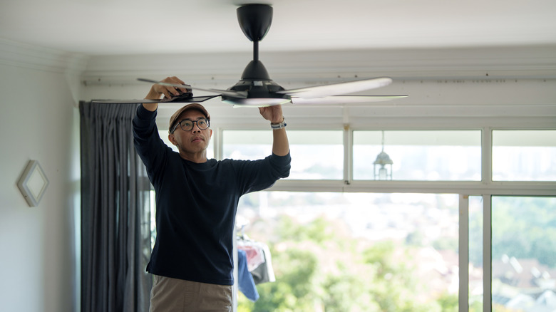 Person cleaning ceiling fan with sponge